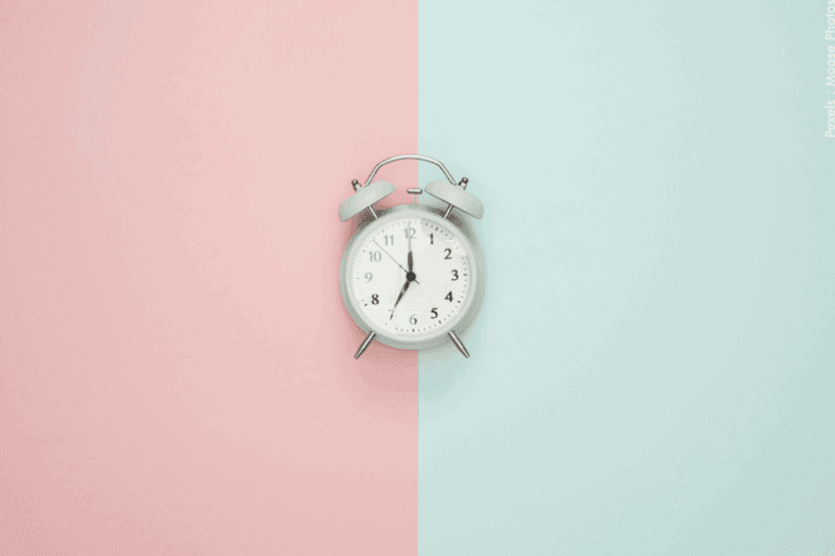 Une horloge ronde vintage sur un fond rose pastel et bleu.