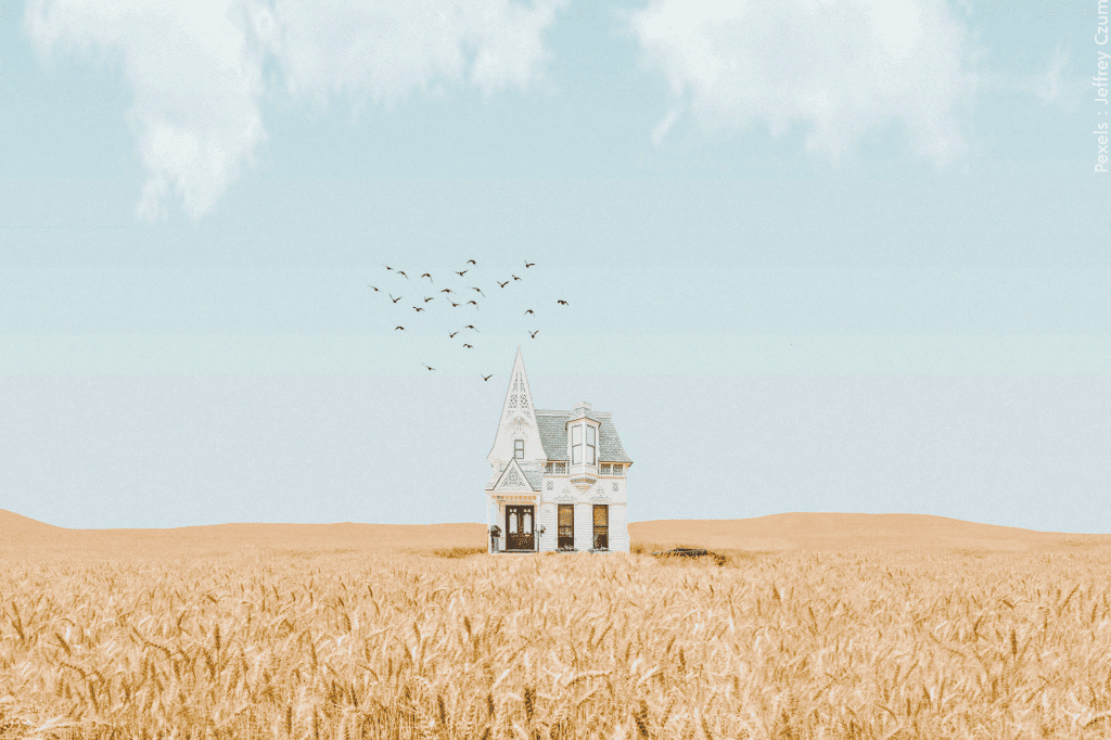 Une maison blanche isolée dans un champ de blé doré, avec un ciel bleu vibrant et des nuages cotonneux au-dessus.